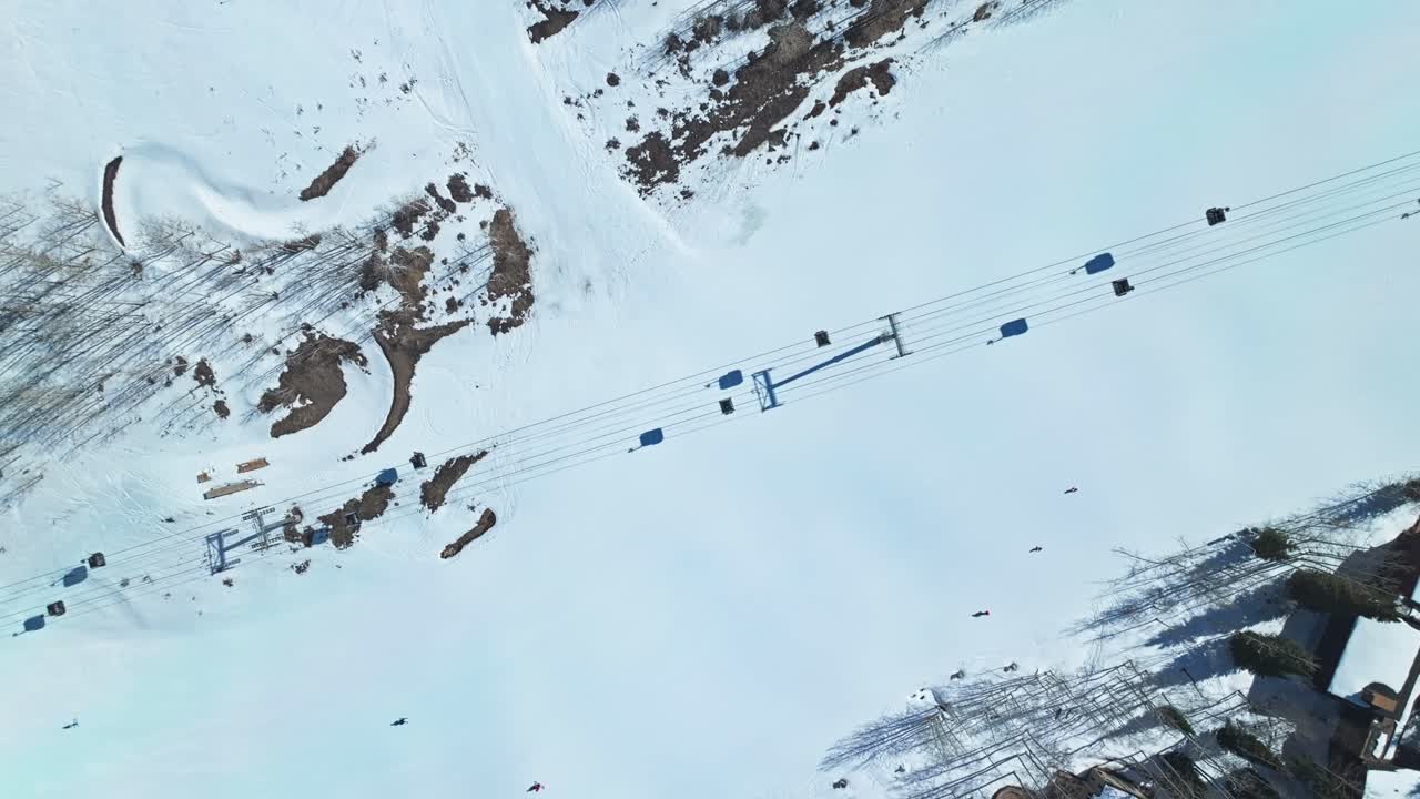Open ski run under clear sky with ridges and scattered pines surrounding the snowy terrain, drone descends on ski lift and skiers, Snowmass Colorado USA