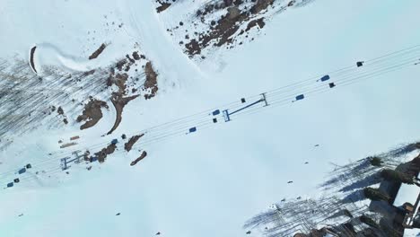 open ski run under clear sky with ridges and scattered pines surrounding the snowy terrain, drone descends on ski lift and skiers, snowmass colorado usa