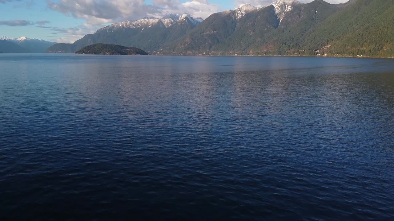 Aerial of BC snow-capped mountains with ocean foreground tilt up