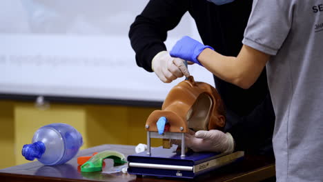 practical skills for medical students. instructor helps practitioner to do a medical procedure into a nose on dummy's head.