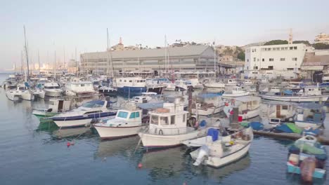 ascending aerial clip of jaffa harbor and jaffa cityscape with boats with clear blue skies and tel aviv skyline at the far background