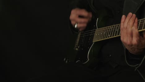 isolated in dark room, man in black plays green sg electric guitar