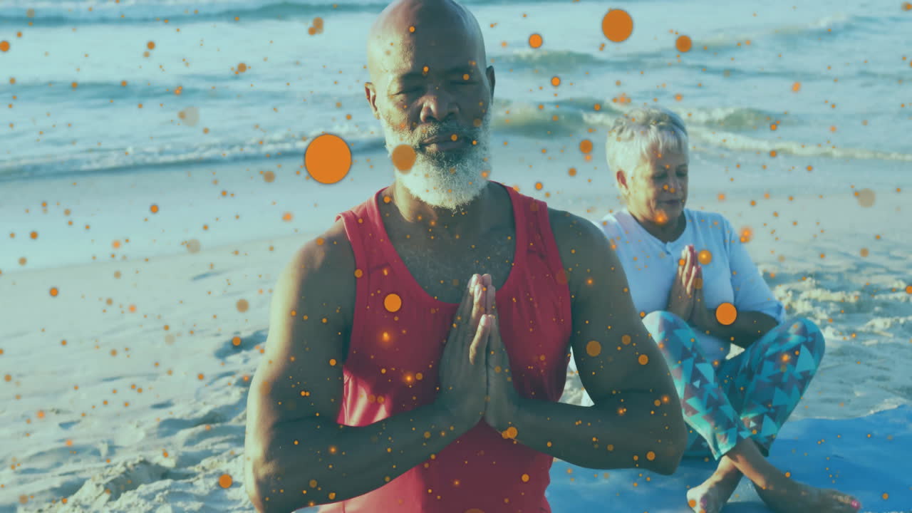 Elderly couple practicing yoga on beach with orange particles animation overlay