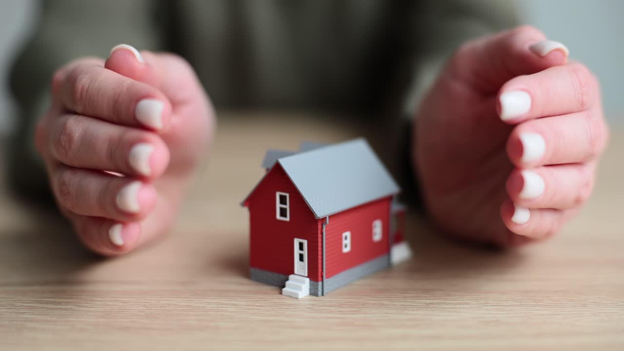 Vrouw legt beschermend haar handen op de zijkanten van een huismodel op tafel.