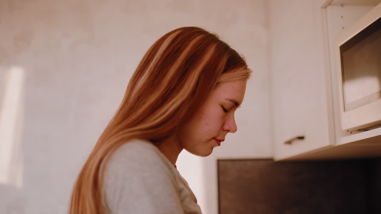 Close up of young woman retrieving coffee container from upper kitchen cabinet with focused look on her face while preparing breakfast in bright morning light