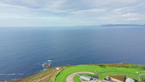 Drone-flying-towards-rural-green-viewpoint-field-on-top-of-a-cliff-with-ocean-in-horizon