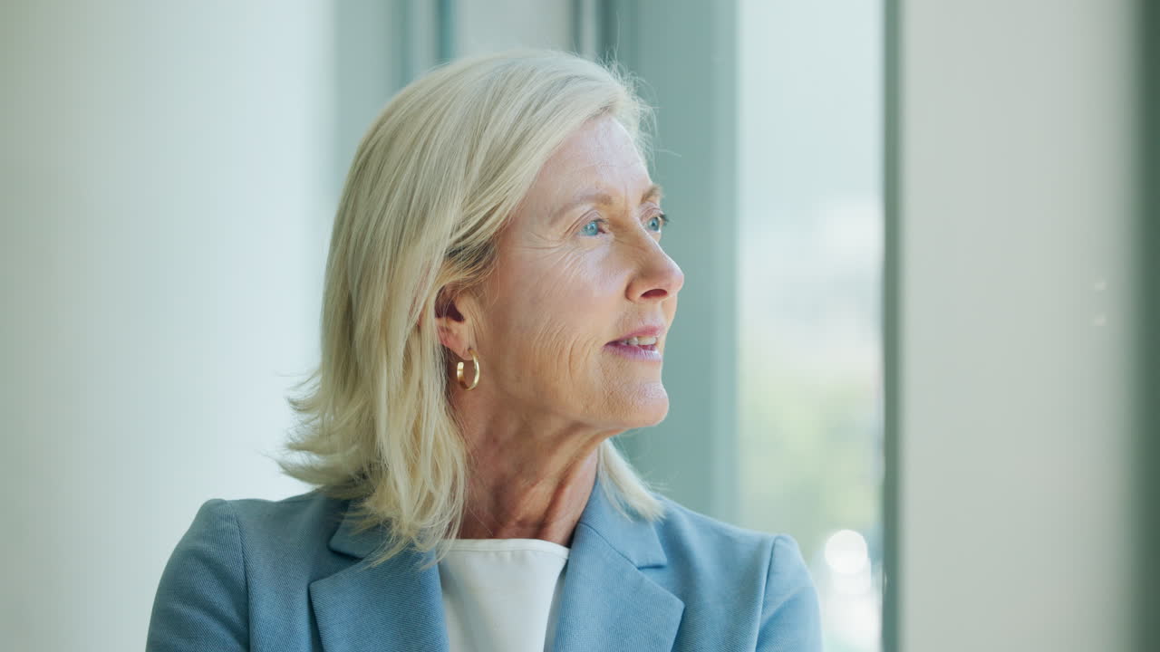 Donna d'affari senior che guarda fuori dalla finestra con espressione pensierosa