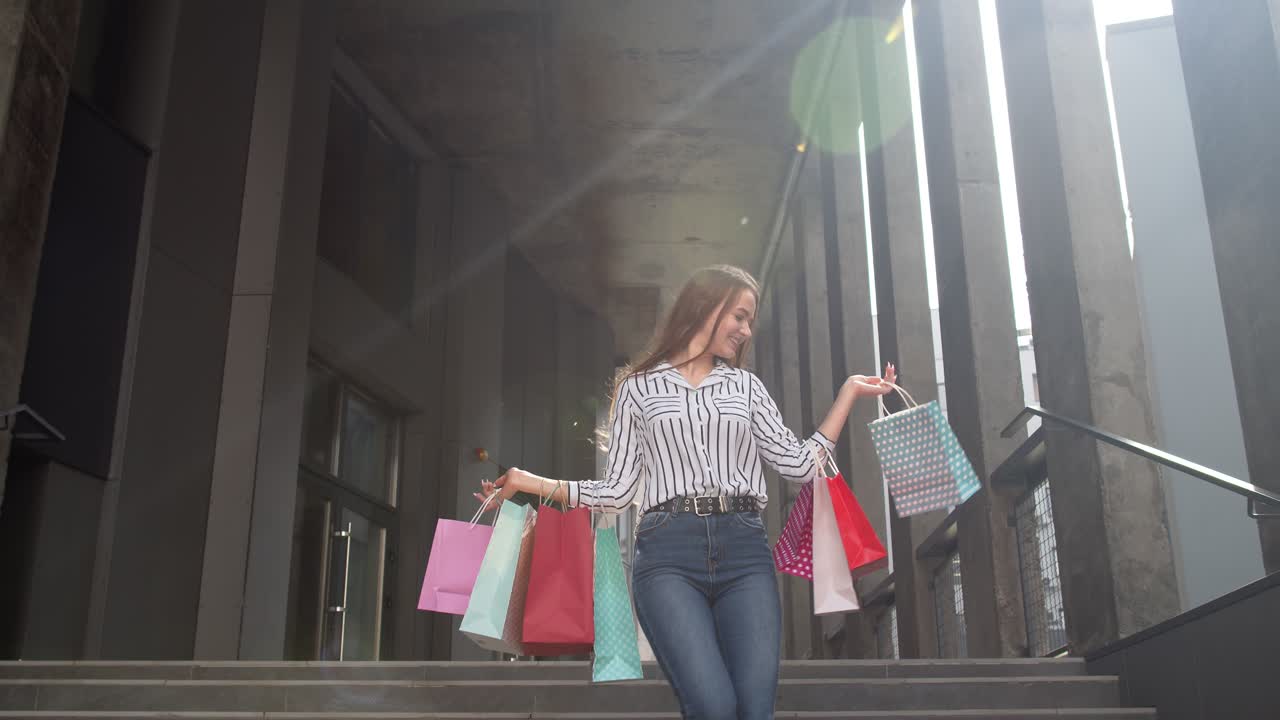 chica sonriente caminando desde el centro comercial con bolsas de compras, feliz con la compra en el viernes negro