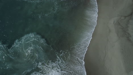 Aerial-shot-of-waves-crashing-on-a-beautiful-sandy-beach-in-Laguna-Beach,-California