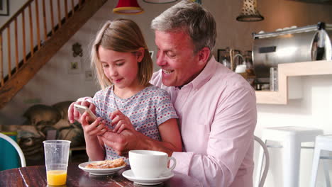 Father-and-daughter-using-a-smart-phone-at-a-table-in-a-cafe