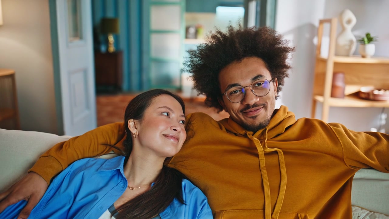 Mixed race couple relaxing on sofa. Happy young pair resting at cozy home.