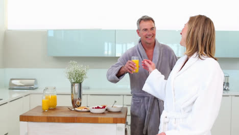 mature smiling man bringing his wife a glass of orange juice at breakfast