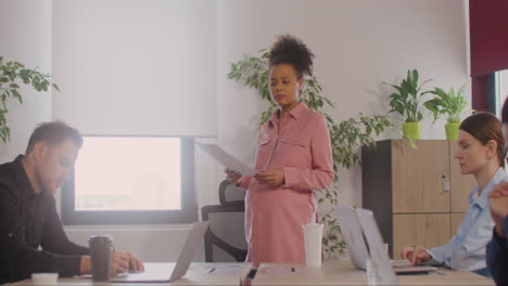 pregnant woman explaining a project in front of her coworkers in a meeting room 7