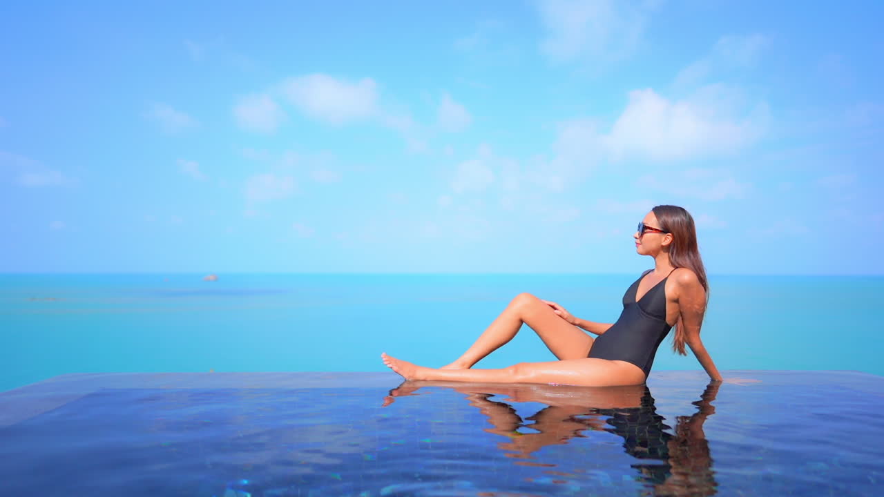 Woman relaxing on the border of rooftop infinity pool with endless seascape on cloudy sky background daytime