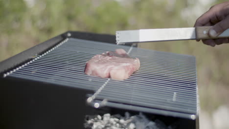 close-up of barbecue grill and metal tweezers putting steak