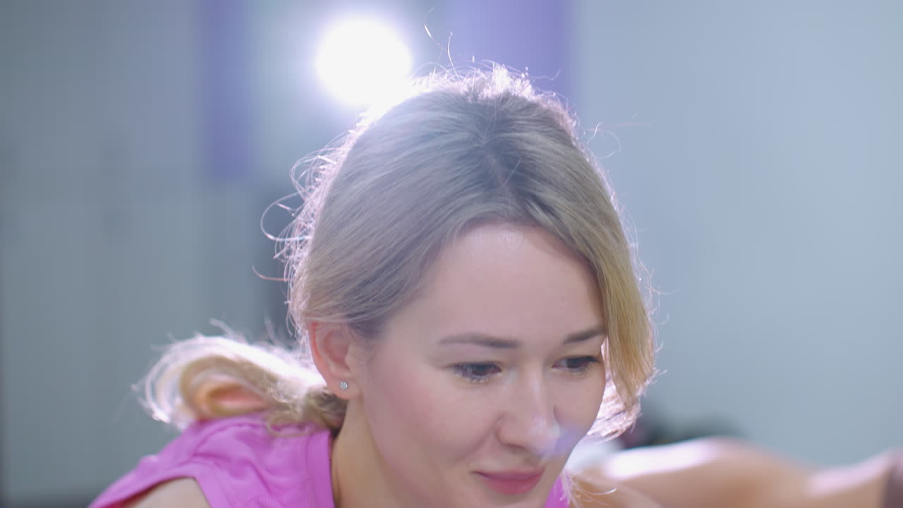 집중된 여성이 강렬하게 운동하고, 앞으로 밀고, 빛이 그녀의 머리를 비추고, 다른 사람의 다리가 근처에 부분적으로 보입니다.