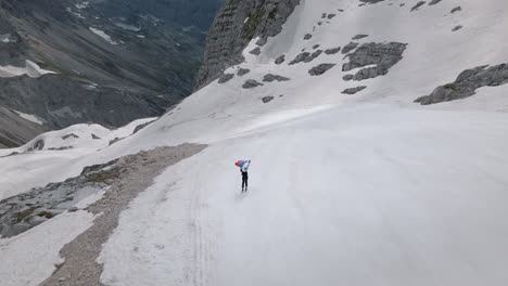 drone shot of mountain kanin, a skiier holding a sloveinan flag above her head and skiing downhil away from a man