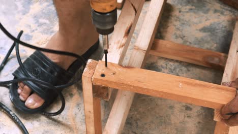 skillfull carpenter employing a power drill to attaching screws into a small wooden chair in his small business workshop to sell and support the local economy