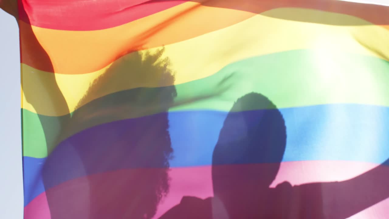 siluetas pareja de lesbianas que sostienen la bandera del arco iris del orgullo en cámara lenta