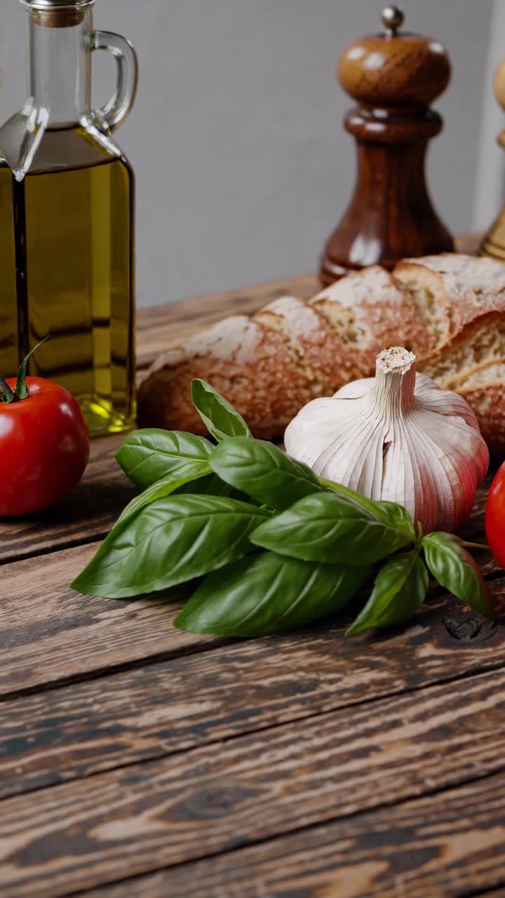 Natura morta video rustica con aglio, basilico, pomodoro e pane su un tavolo di legno.