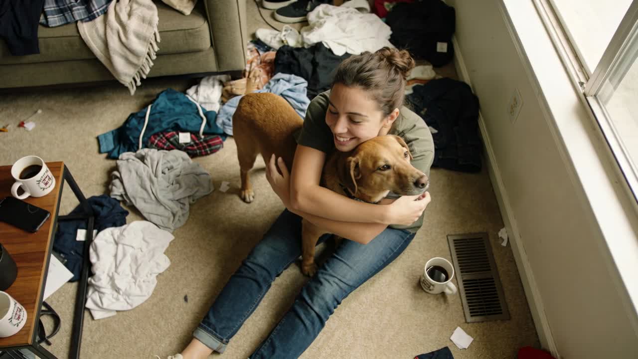 Hugging woman in green tee holding brown dog after dog approaching in apartment, with mugs phone