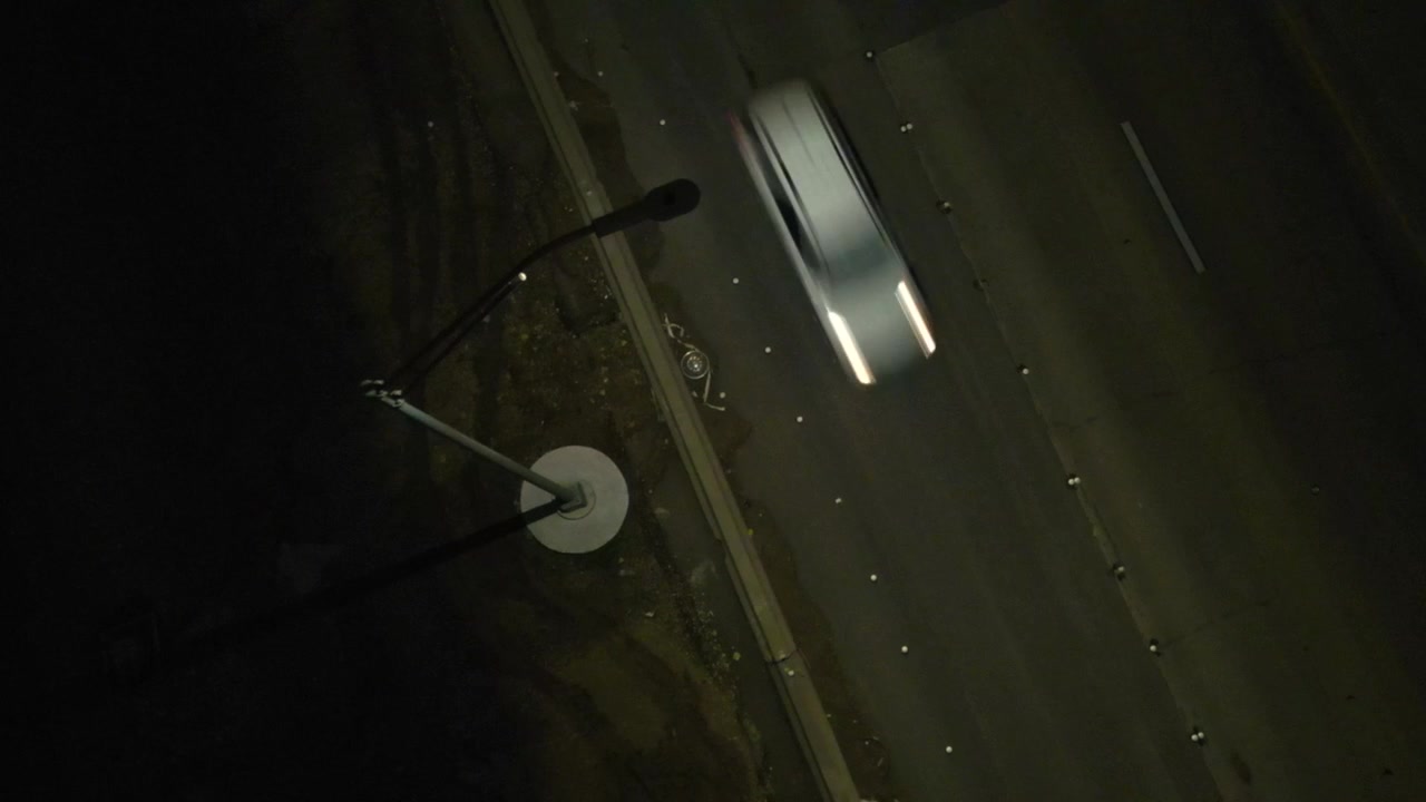 Un faro a palo alto sfarfalla su un'autostrada mentre camion e auto passano sotto