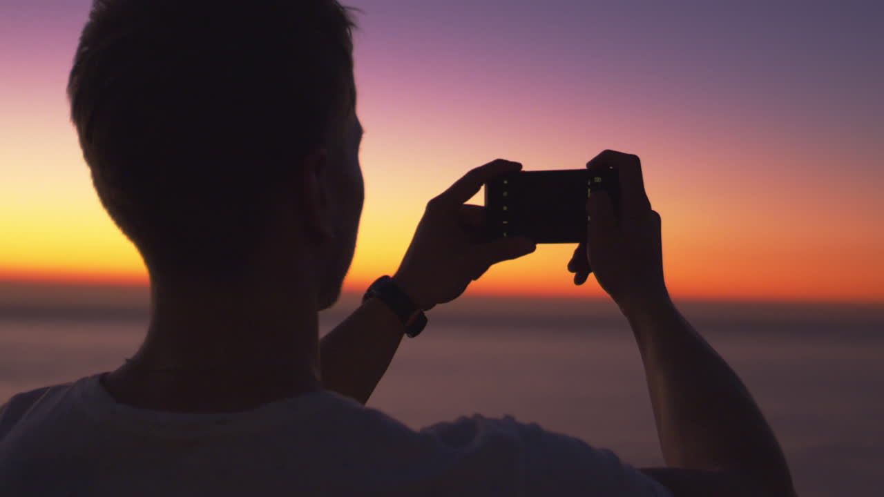 hombre tomando una foto panorámica con el teléfono en una playa al atardecer