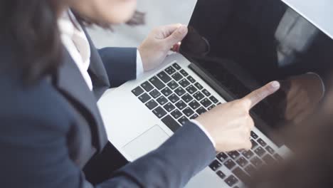 Female-Businesswoman-Using-Laptop-Computer,-Typing-And-Pointing-At-Display-While-Sitting-Outside-With-A-Colleague