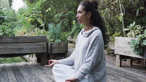 focused biracial woman practicing yoga meditation in sunny garden, slow motion