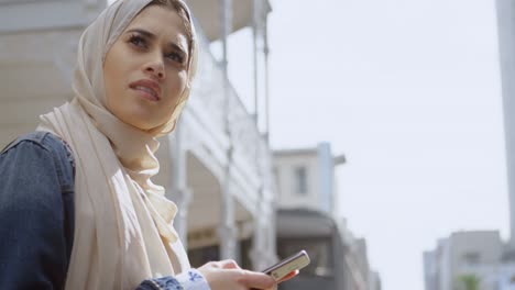 animación de una mujer asiática en hijab sentada y usando un teléfono inteligente sobre el paisaje urbano