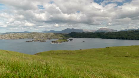 a wide landscape view of the mountains and rocky coastline of north scotland with lush green grass and slowly moving clouds, filmed on handa island