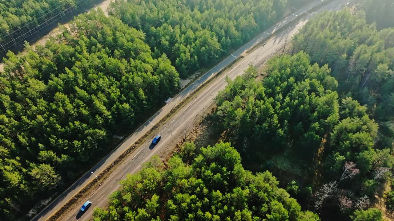 Aerial road view with trucks and cars passing between dense pine forests, Latvia