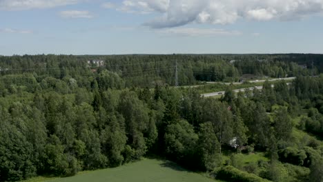 Slow-aerial-pan-of-a-motorway-in-Finland-near-Kerava-lined-by-powerlines-and-trees