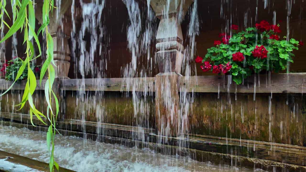 Water cascades over garden pergola with red geranium floral decoration