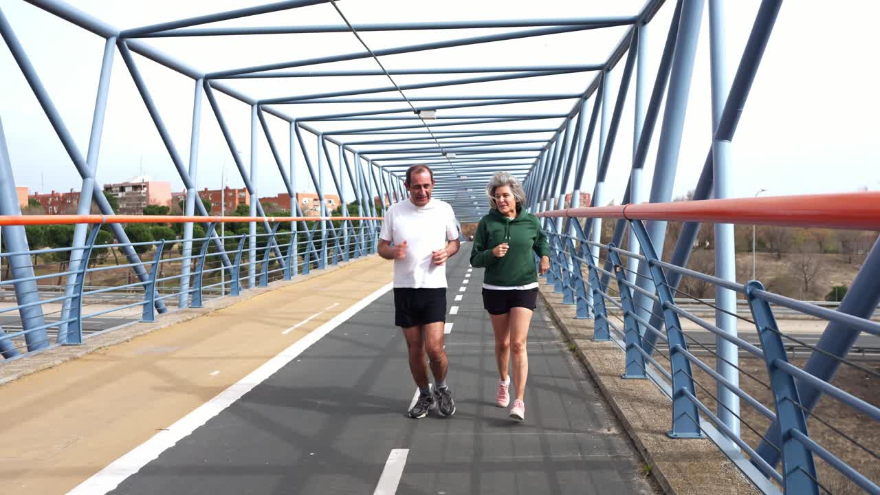 Casal Idoso Feliz Correndo Juntos em uma Ponte Pedonal Moderna