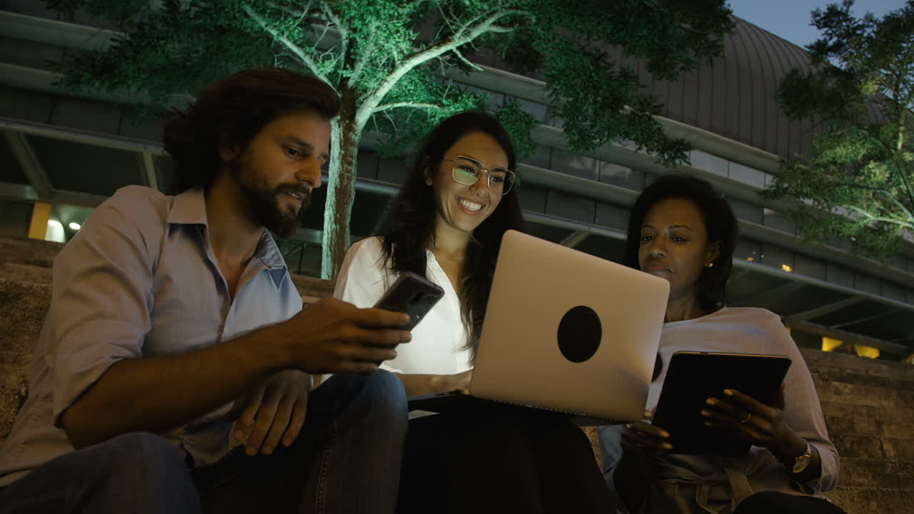 tres jóvenes colegas sentados en las escaleras con dispositivos electrónicos