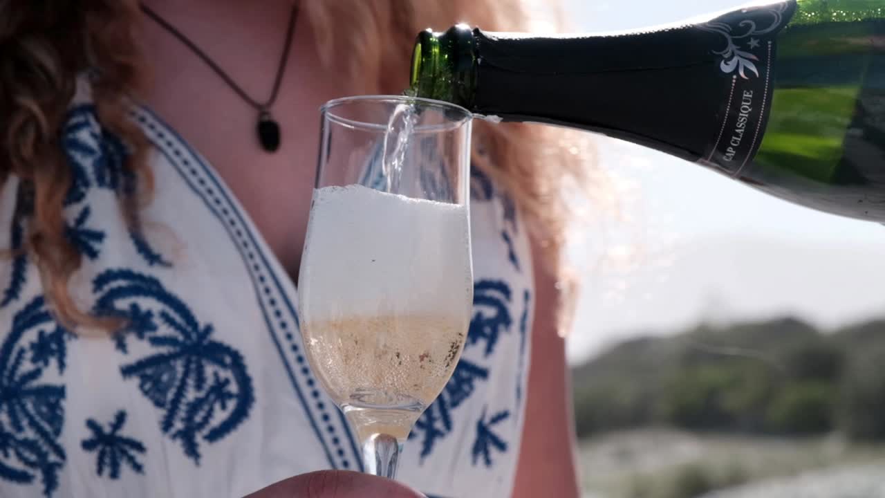Sparkling wine being poured into a champagne glass for a woman at a beach wedding celebration