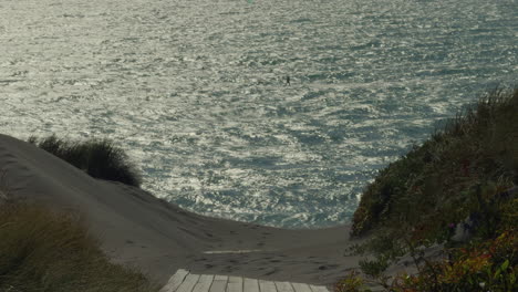 end of empty boardwalk going off into beach with calm ocean in background with silhouette of kite surfers