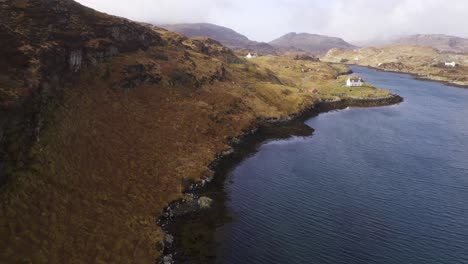 drone shot of a collection of remote, coastal houses with a scottish mountain range, moorland and peatland in the background