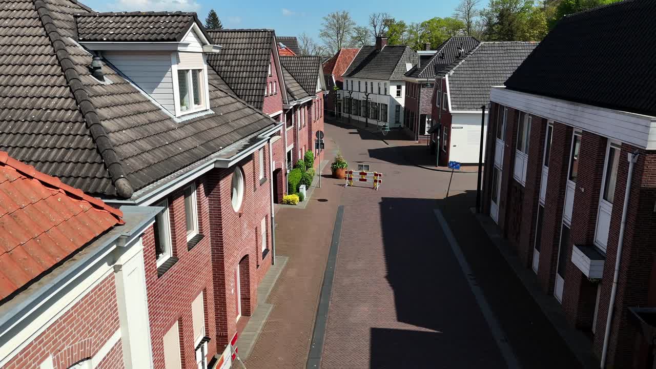 Waving dutch flag on house wall of small city of Netherlands. Aerial forward shot. Hanging Lantern Lamp between historic red brick two-story houses. Sunny day in spring season.