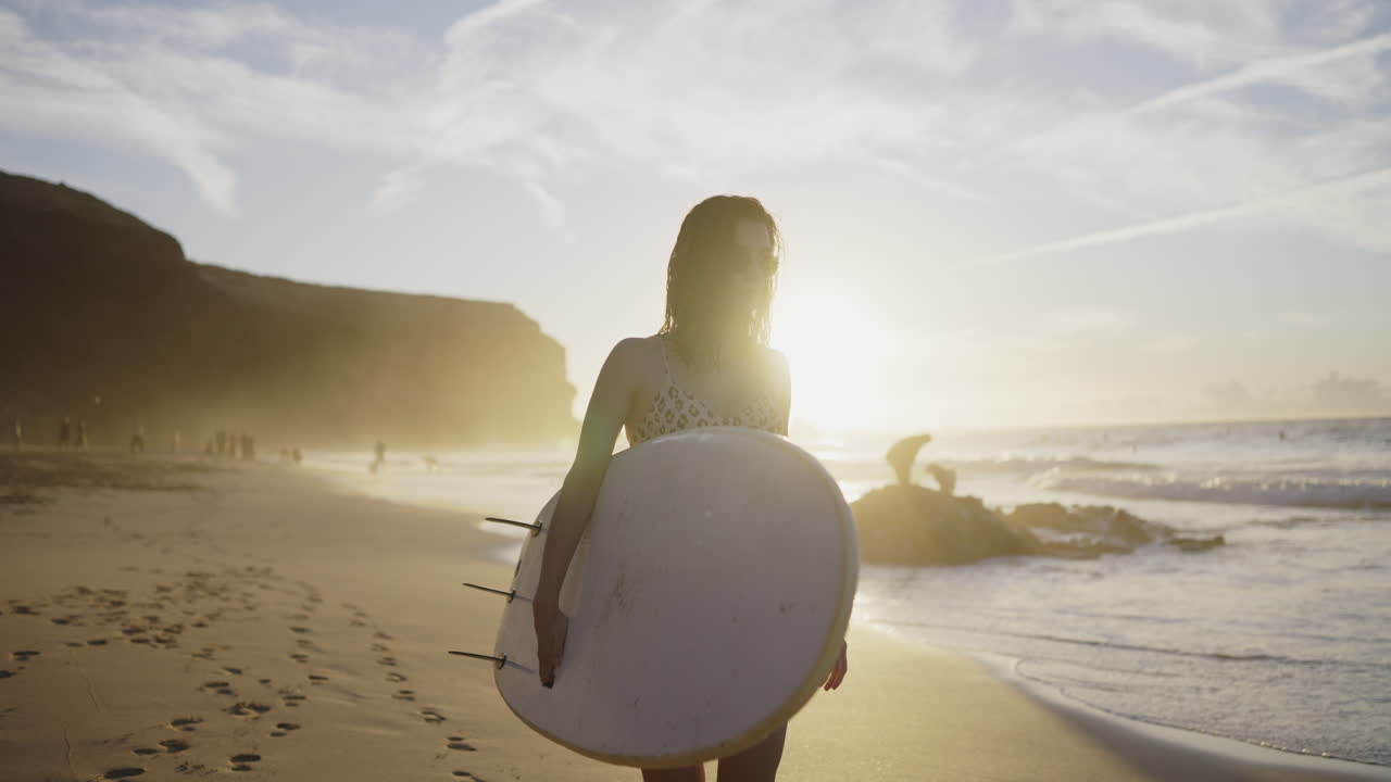 Woman with surfboard on beach at sunset