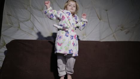 Little-cute-girl-with-blond-hair-jumps-on-sofa.-Bathrobe-clothes.-Happy