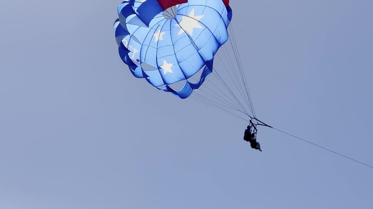 Un paracadute blu e bianco con motivo a stelle scivola in un cielo terso sopra l'oceano