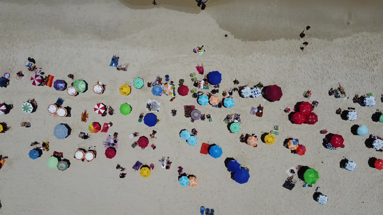 drone con cámara 90 grados abajo con movimiento lateral filmando varios paraguas coloridos y personas en la playa de ipanema, brasil