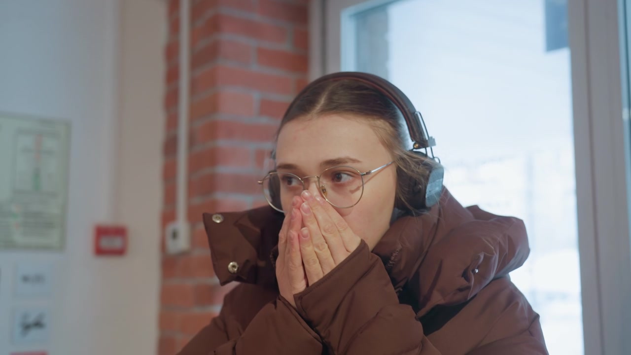 Jonge vrouw in winterjas en koptelefoon komt een warme plek binnen.
