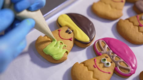 gloved hands squeeze the creamy decoration from pastry bag on the cookies of mushroom shape. biscuits icing on the tray. close up.