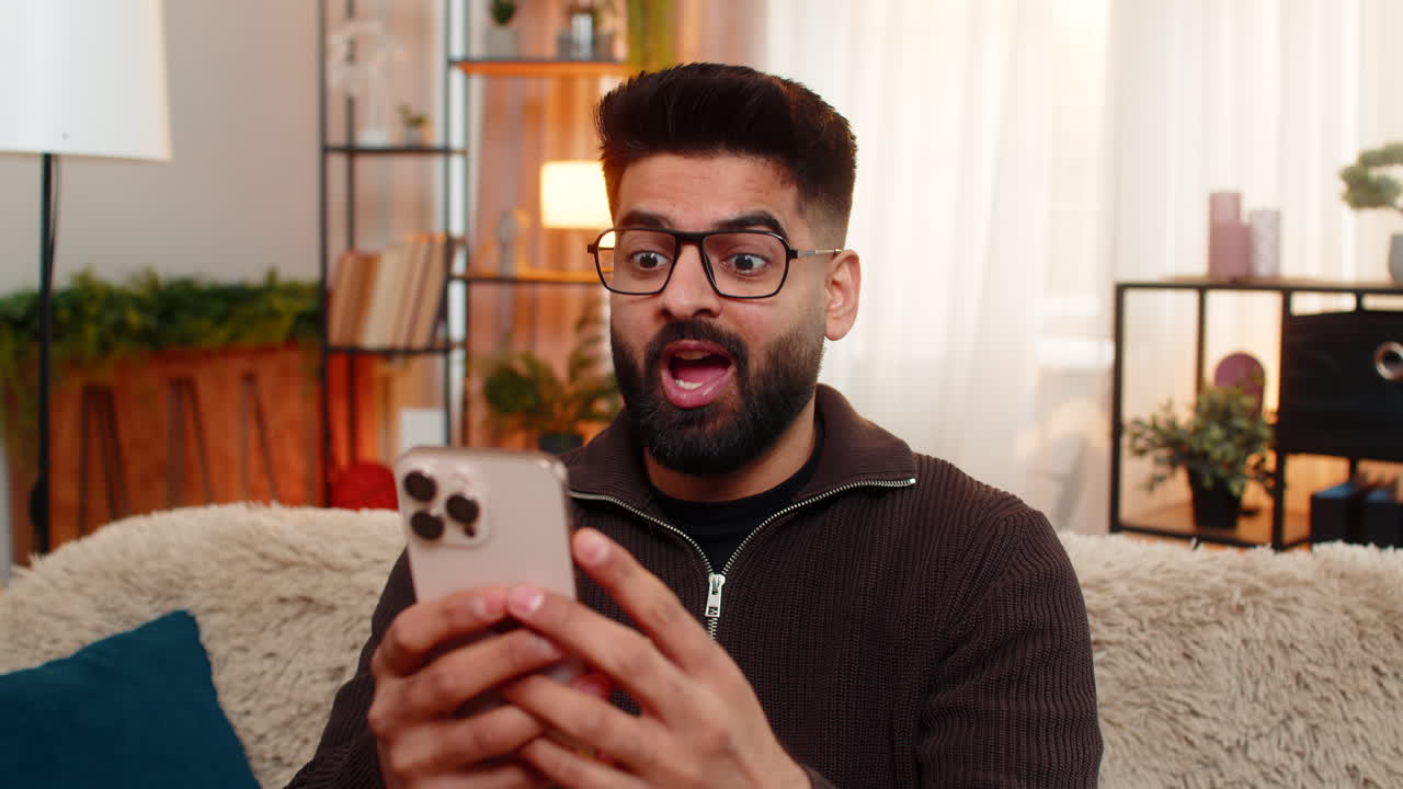 Indian happy man at home shocked while reading good news on smartphone surprised happy reaction