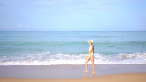 Mujer-Asiática-Adulta-En-Traje-De-Baño-Amarillo-Camina-Junto-Al-Mar-En-Una-Playa-De-Arena