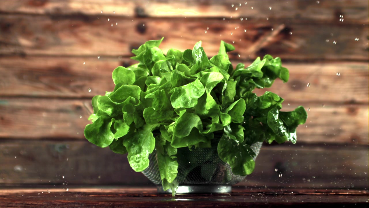 Lattuga verde fresca in uno scolapasta con gocce d'acqua su sfondo di legno.