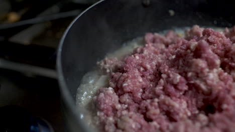 close up shot of sizzling oil bubbling around pan cooking raw mince beef